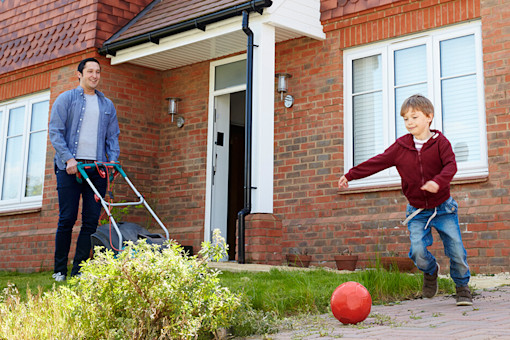 Children play in garden as father mows lawn outside house