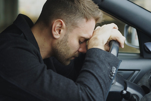 Stressed young man with head on the steering wheel