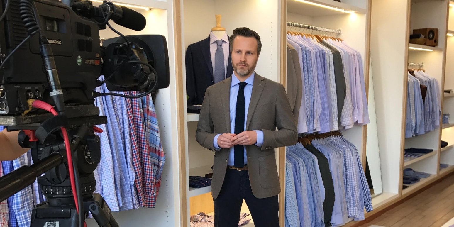 Hero image of a man in a suit store, wearing a suit, talking into a video camera