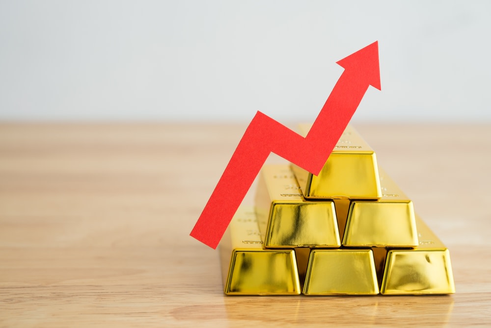 Gold bars stacks and red graph chart growing up on wooden background