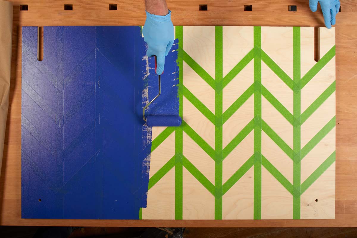 using paint roller to layer dark blue paint over tape