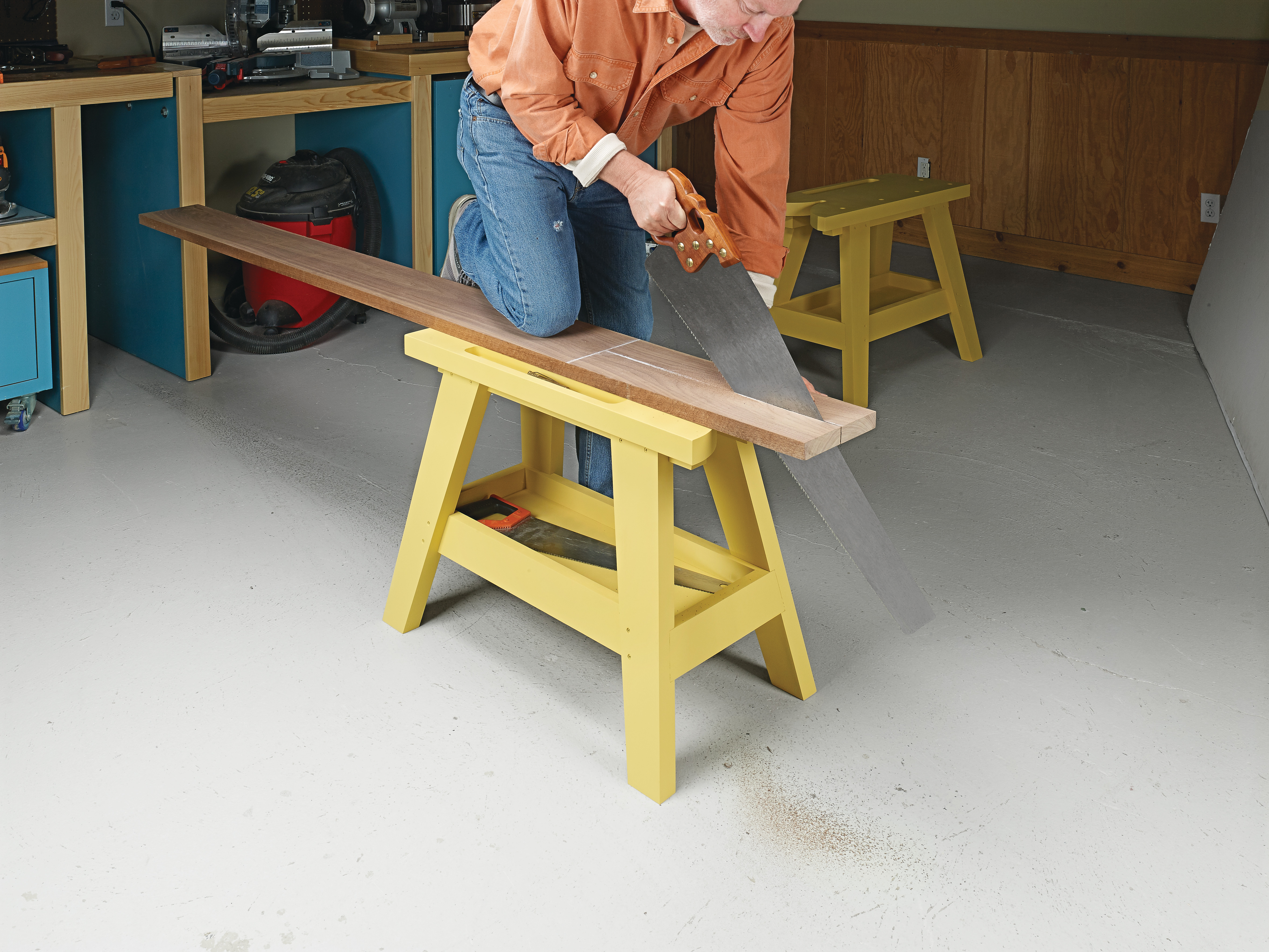 using hand saw to cut wood piece in half on sawhorse