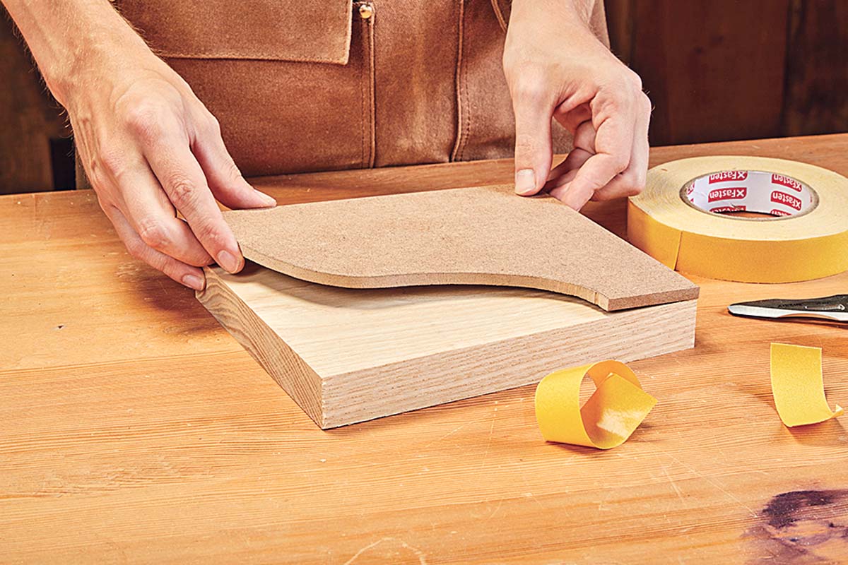 pressing the template down onto wood piece with double-sided tape