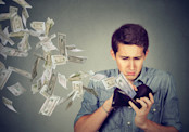 Sad man watching money fly out of wallet