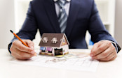 Architect Drawing on Plan with Small Model House on Top