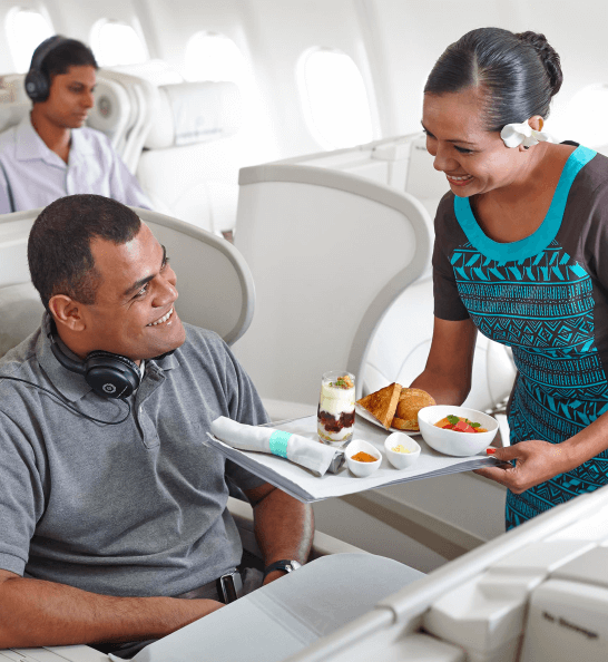 A Fiji Airways flight attendant serves a customer aboard an aircraft.