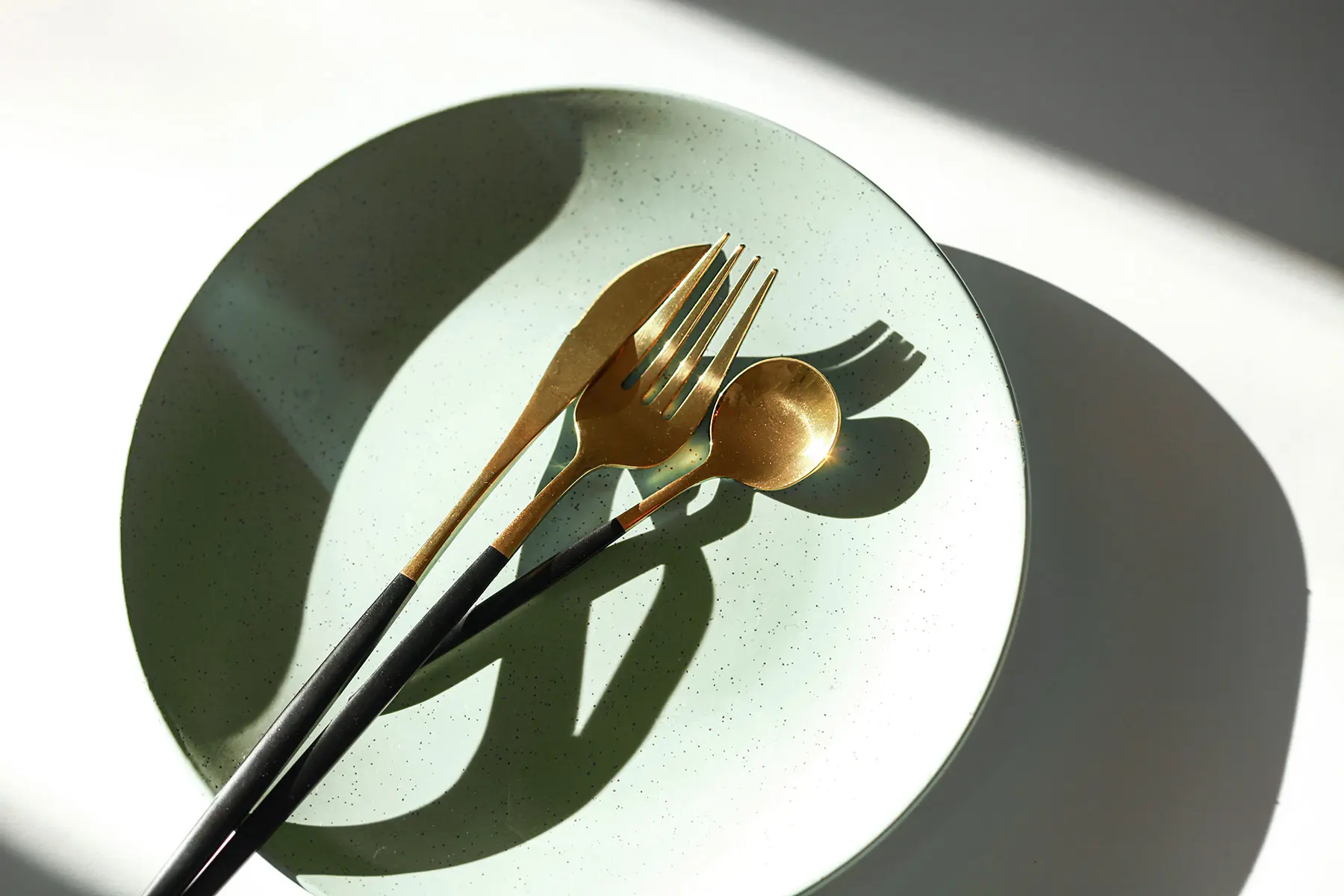 Empty ceramic plate with utensils, strong light with crisp shadows. header