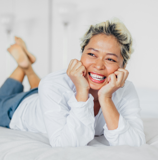 Asian woman with bleached blonde hai lying on bed, smiling off camera resting on elbows.