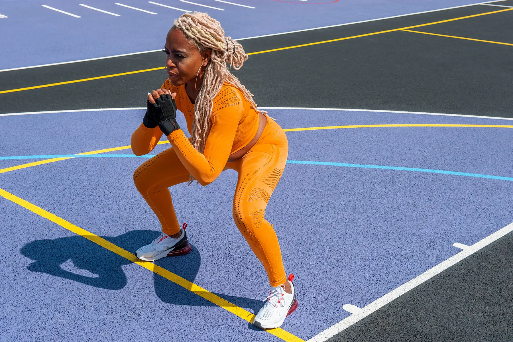 Fit, middle aged Black woman with blond dreadlocks practices compound resistance exercise on an outdoor track in gym outfit. header