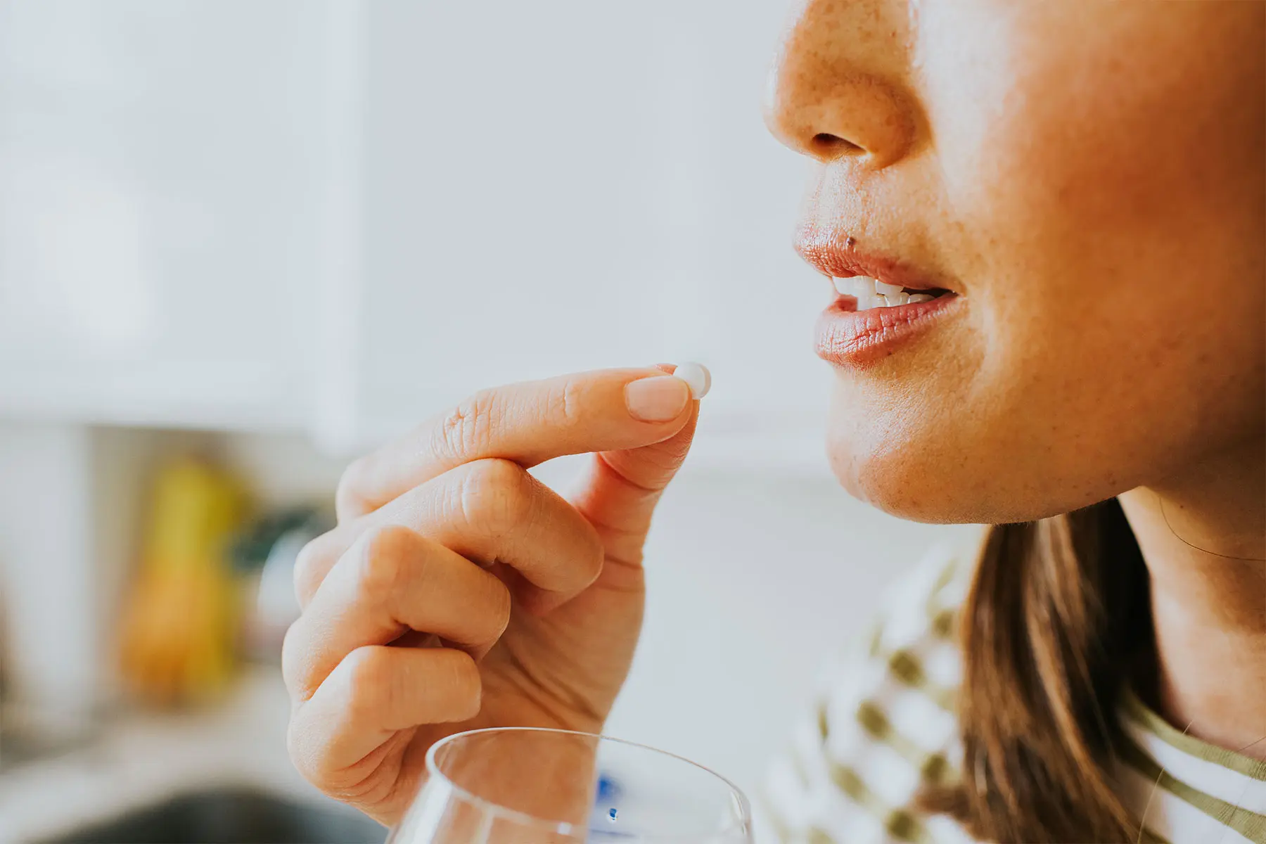 Close up of a woman in profile, about to swallow Estradiol tablet with a sip of water. header