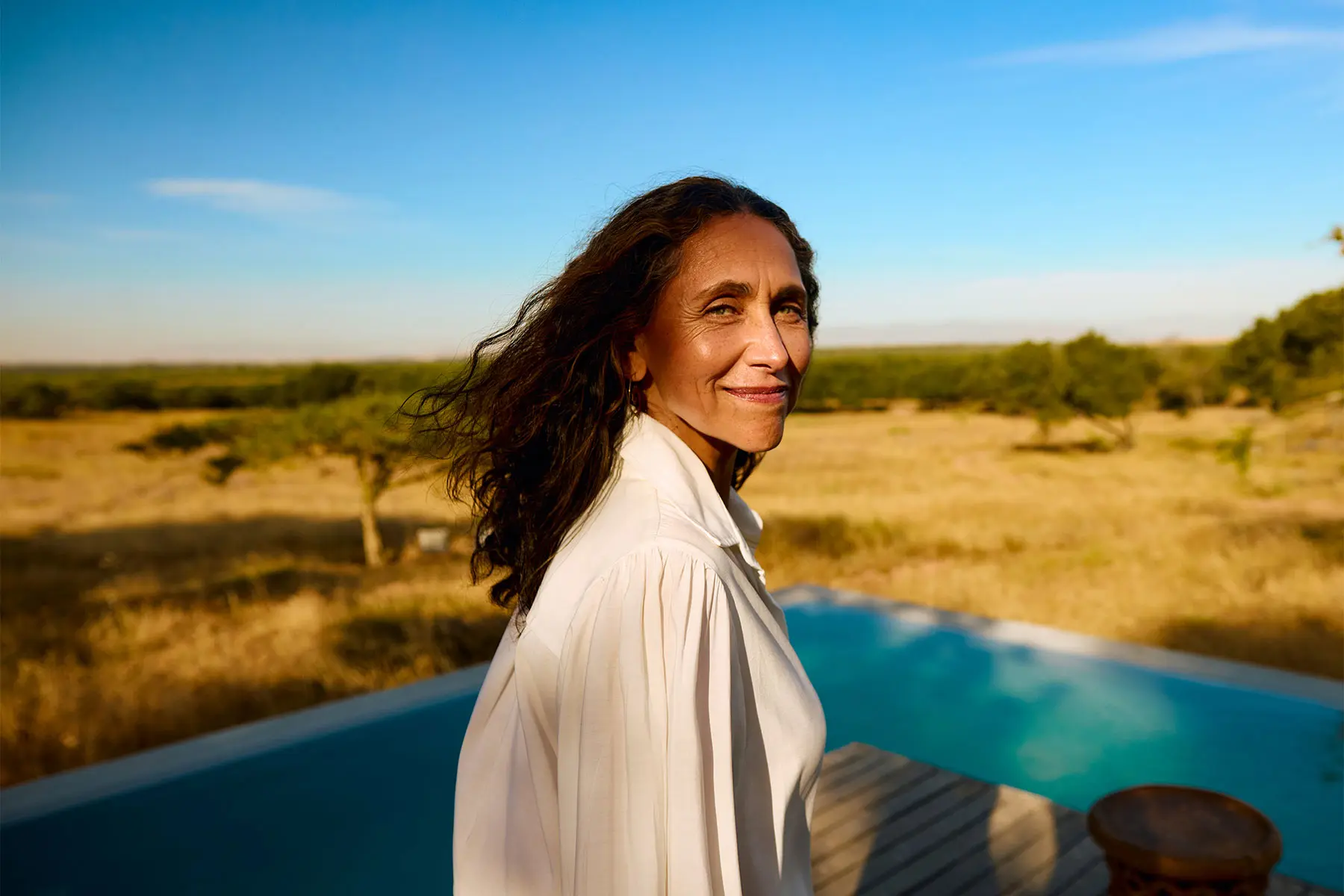 Middle-aged woman in a white button down shirt standing near a swimming pool. header