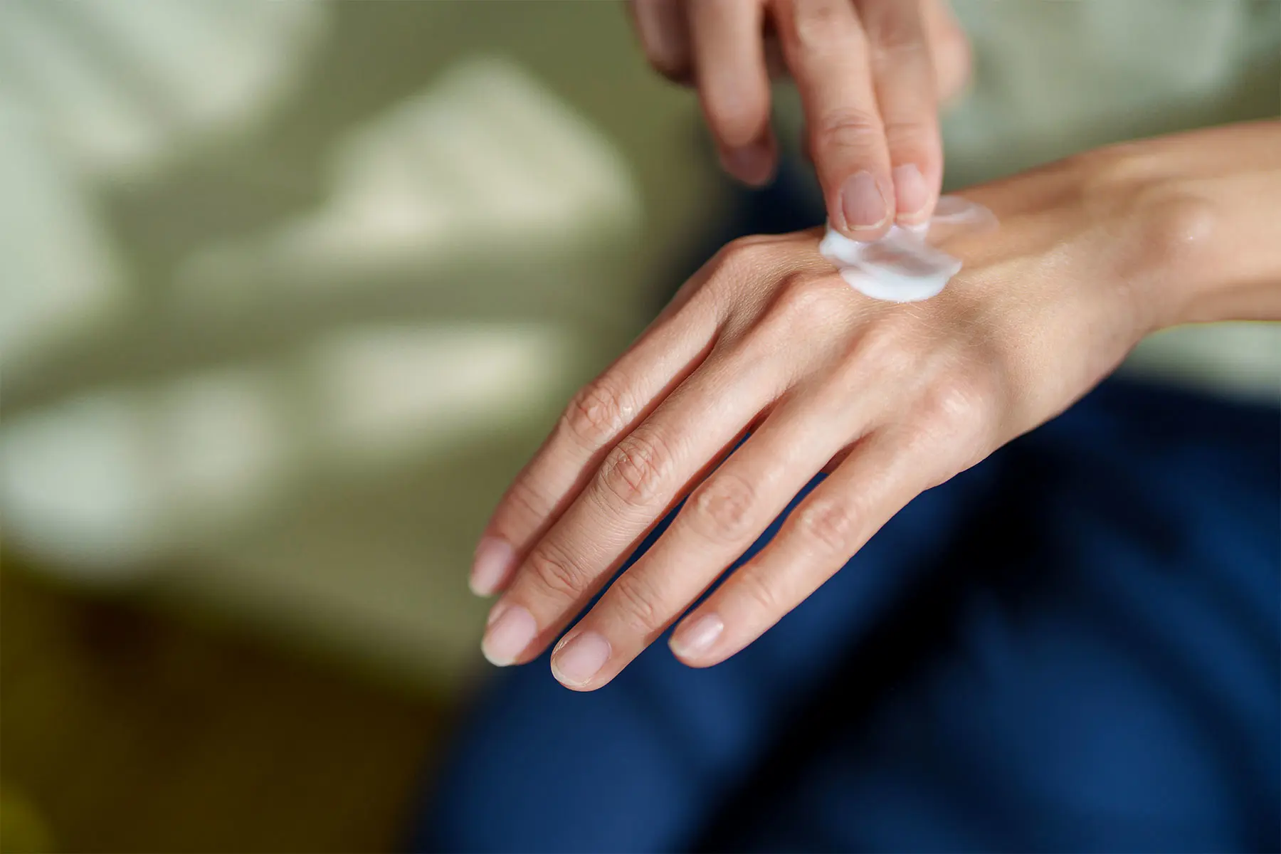 Detail view of a woman applying M4 cream to the top of her hand. header