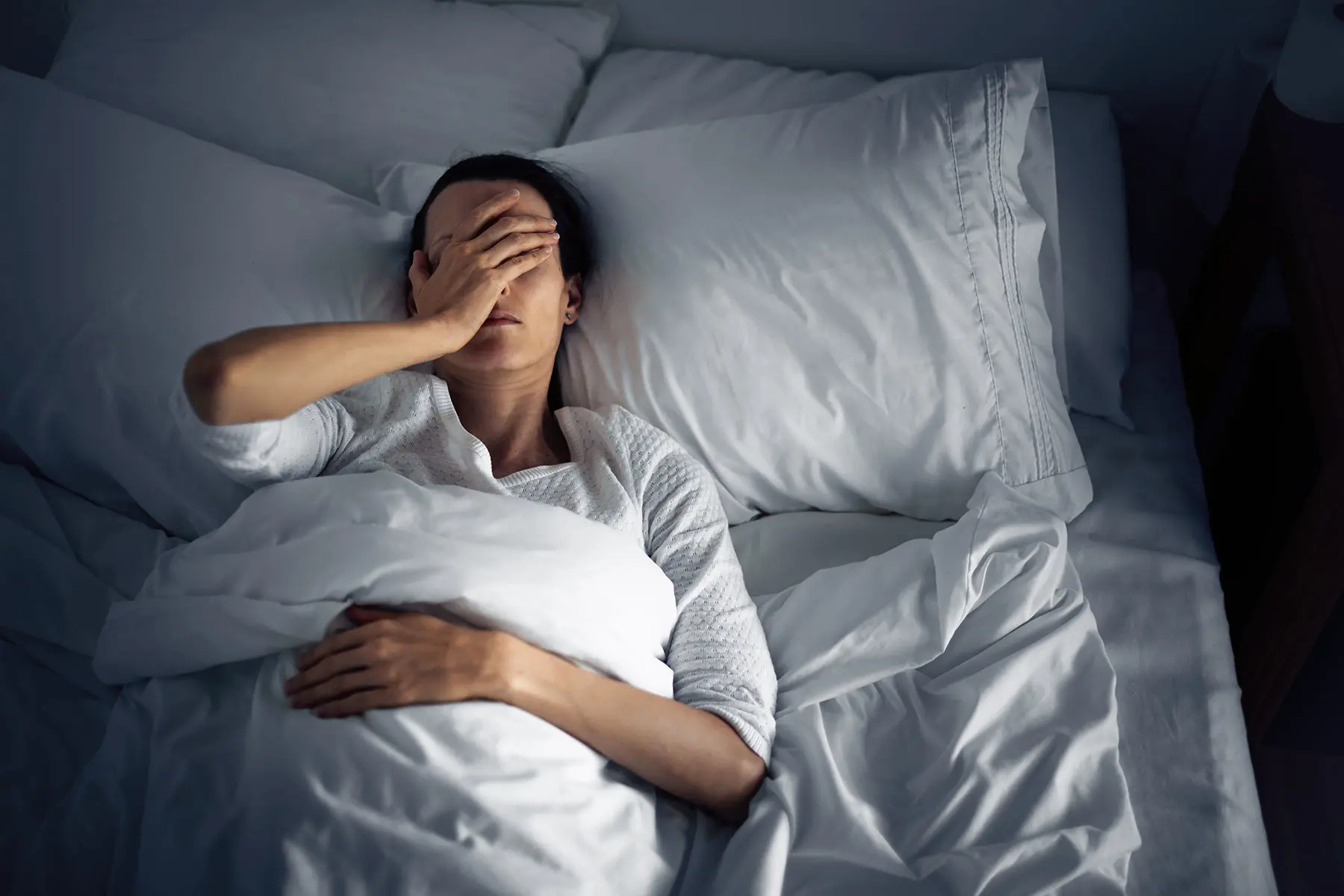 Woman seen from above in bed, struggling with discomfort from heart palpitations.