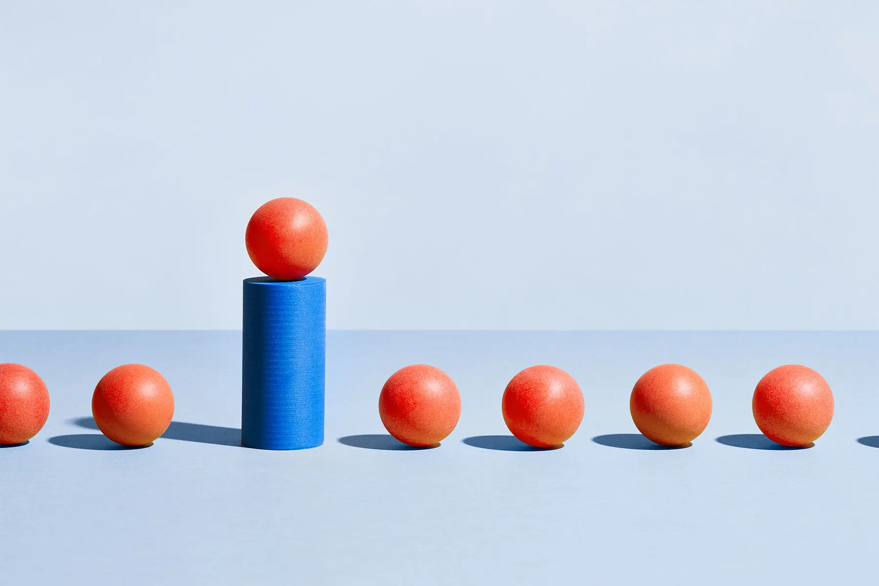 Conceptual photo showing choice and comparison, orange balls with one elevated on blue pillar. header