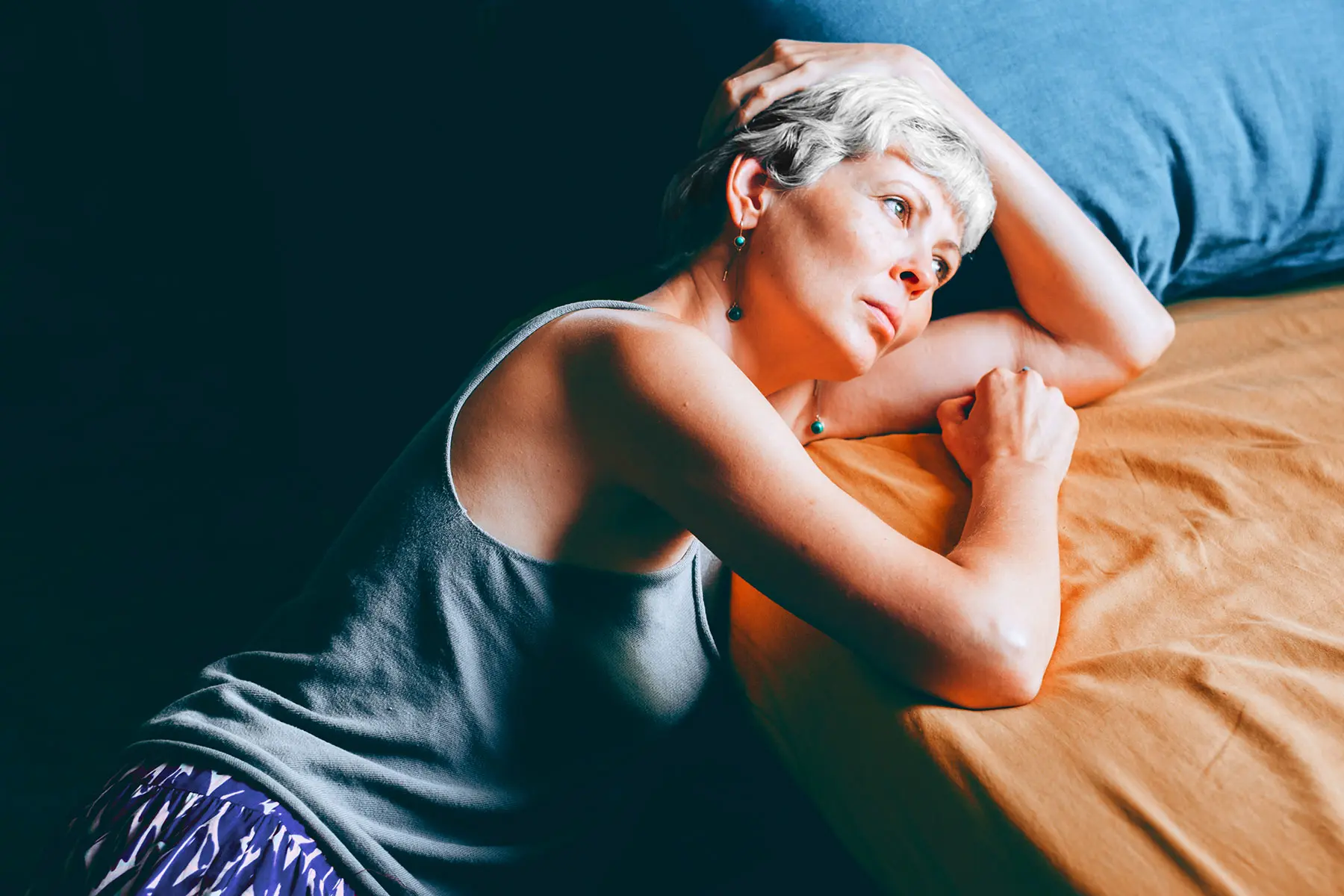 Woman with cropped hair and bangs sitting on the floor in discomfort with sensation of UTI