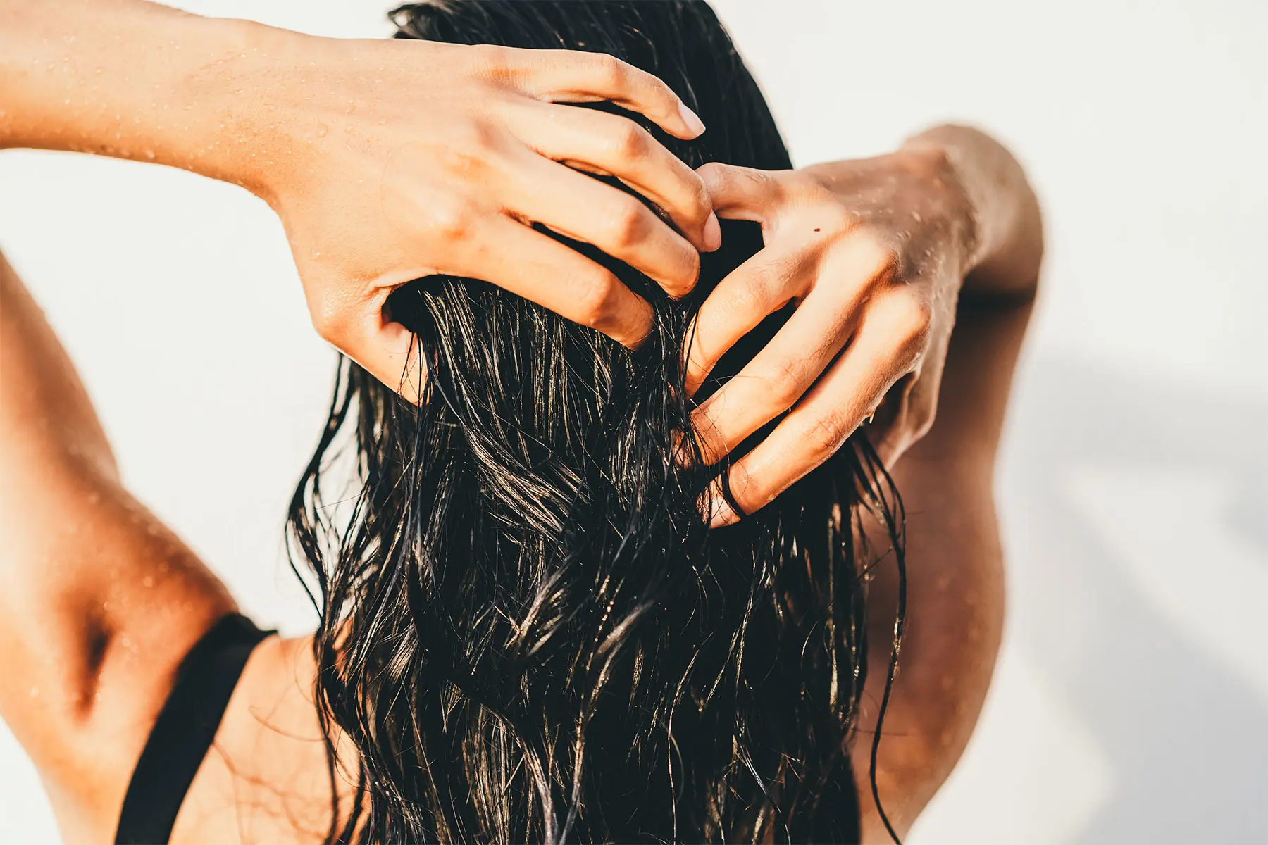 Woman seen from behind drying wet hair with her hands, experiencing shedding. header