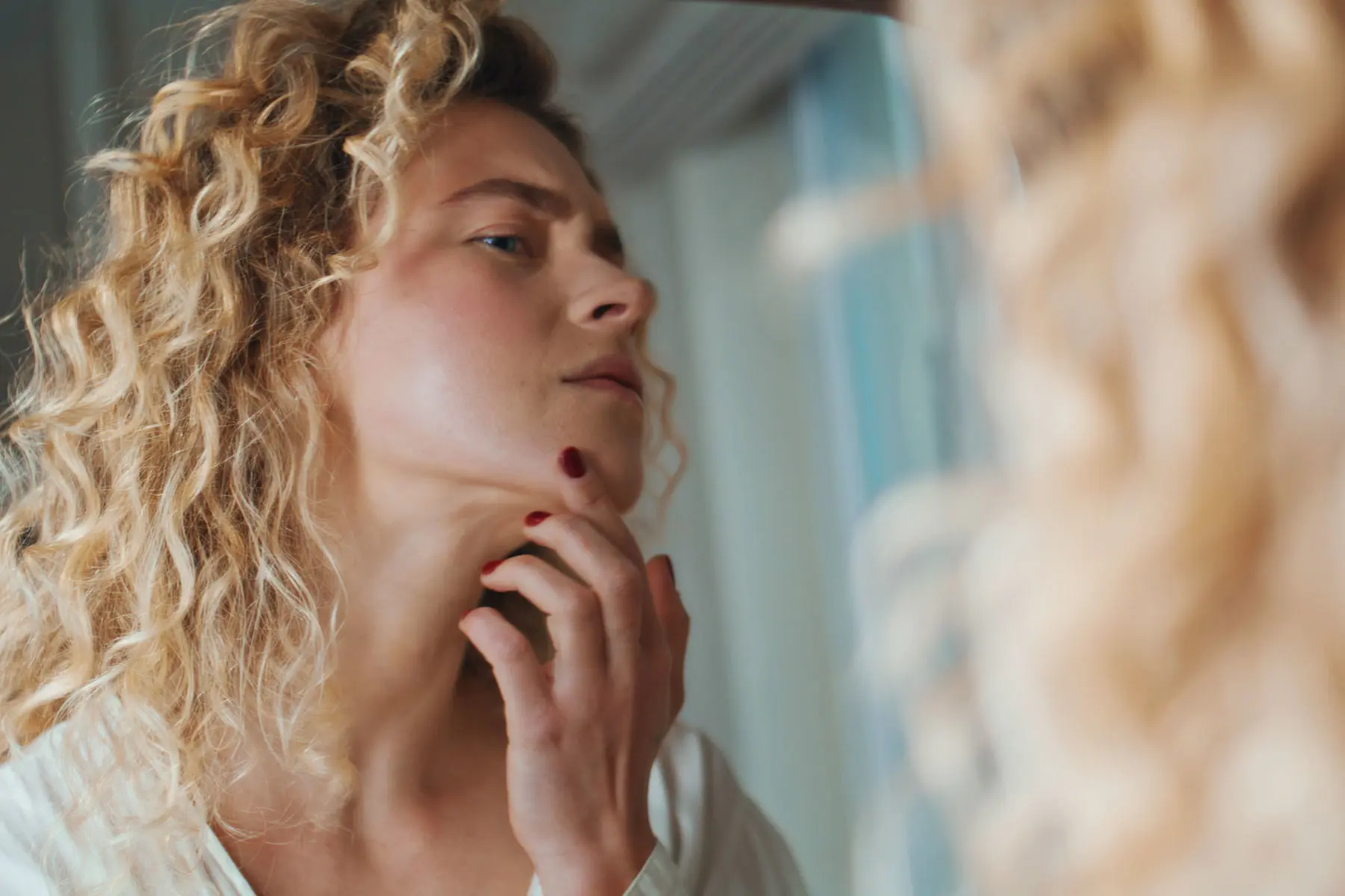 Woman examining facial hair on chin in the mirror. header