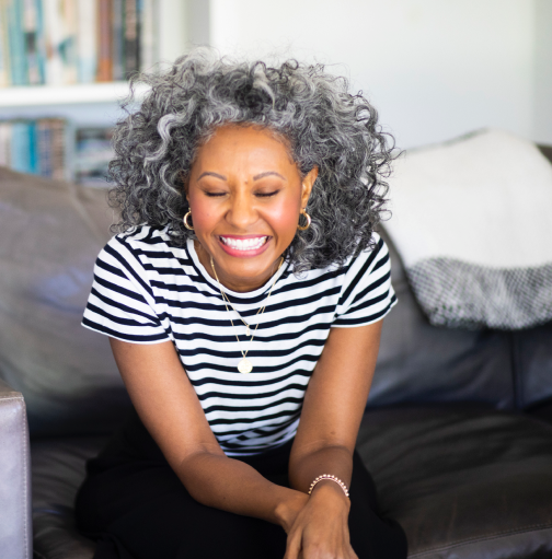 Black woman with curly grey hair in striped shirt eyes closed laughing.