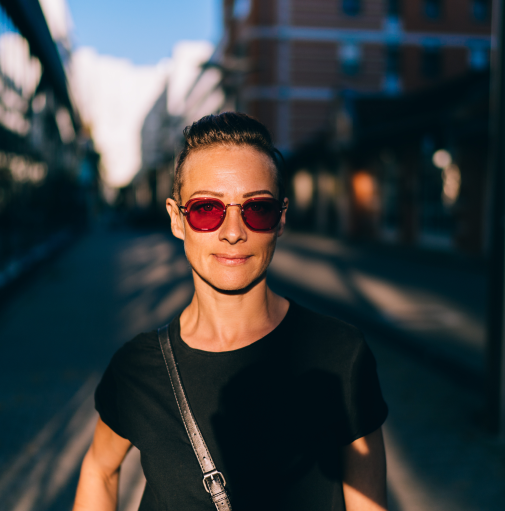 Short haired woman partially cast in shadows of afternoon sun on urban street, wearing sunglasses. AW083 