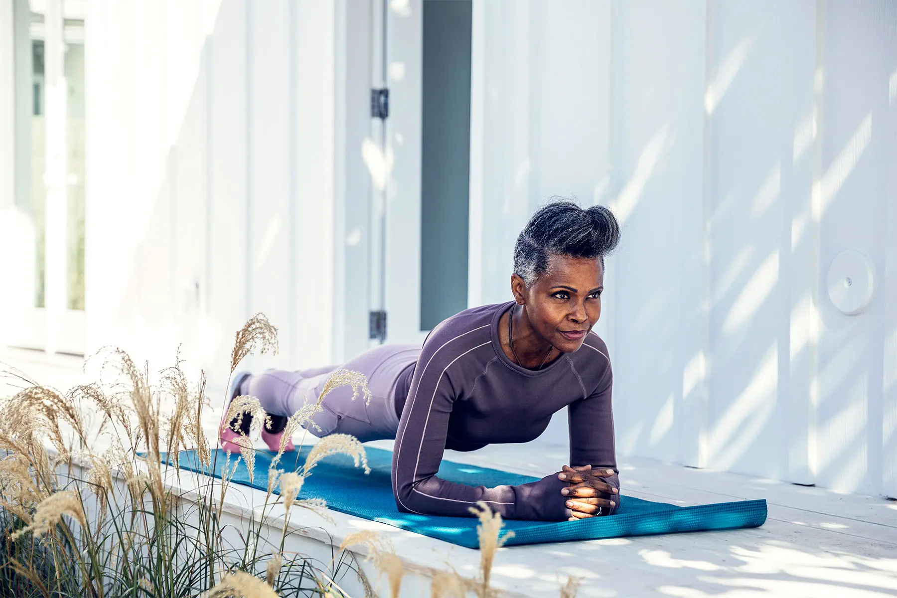Fit looking Black woman holding plank pose on a yoga mat outdoors.