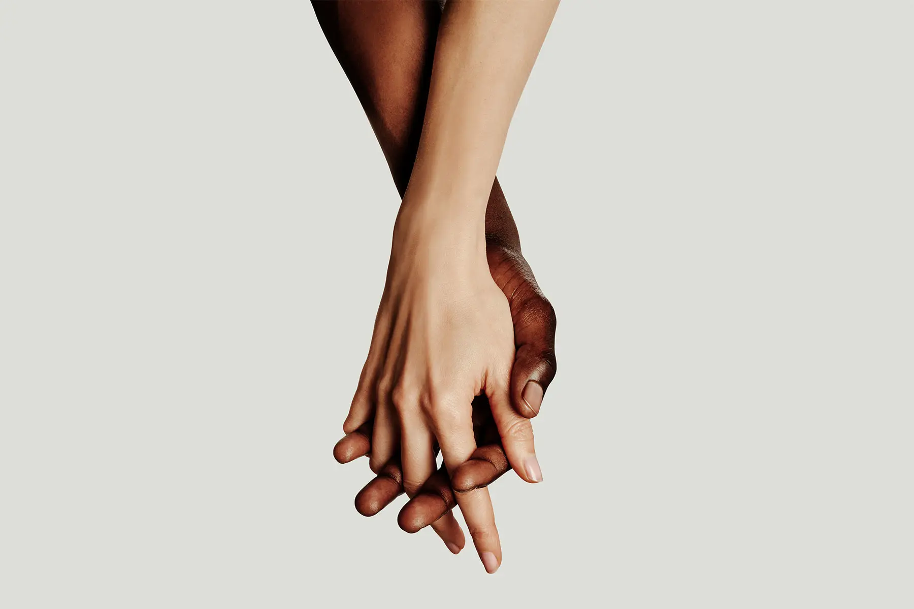 Interracial couples' hands intertwined on studio background header