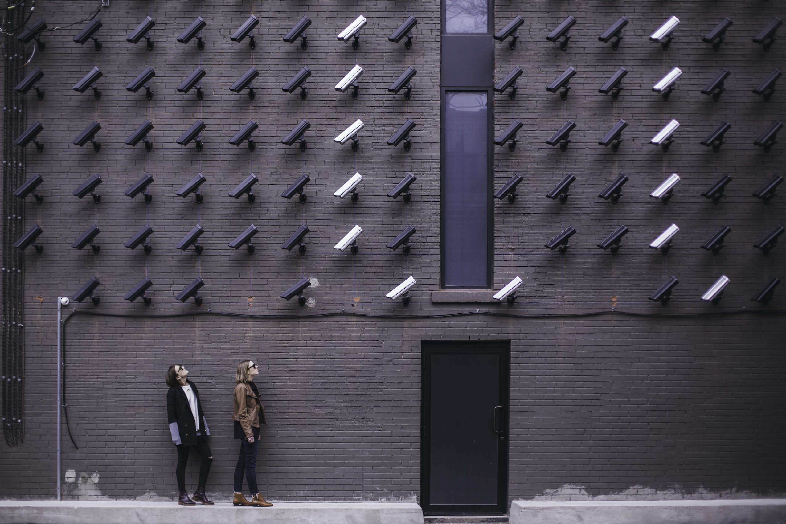 A wall of CCTA cameras watching two women, by Matthew Henry