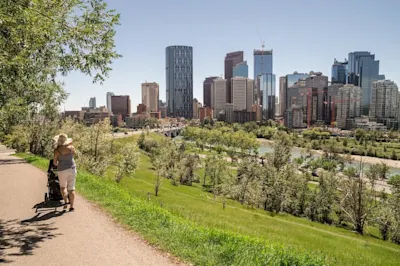 Person pushing a stroller along a path with the Calgary skyline in the background