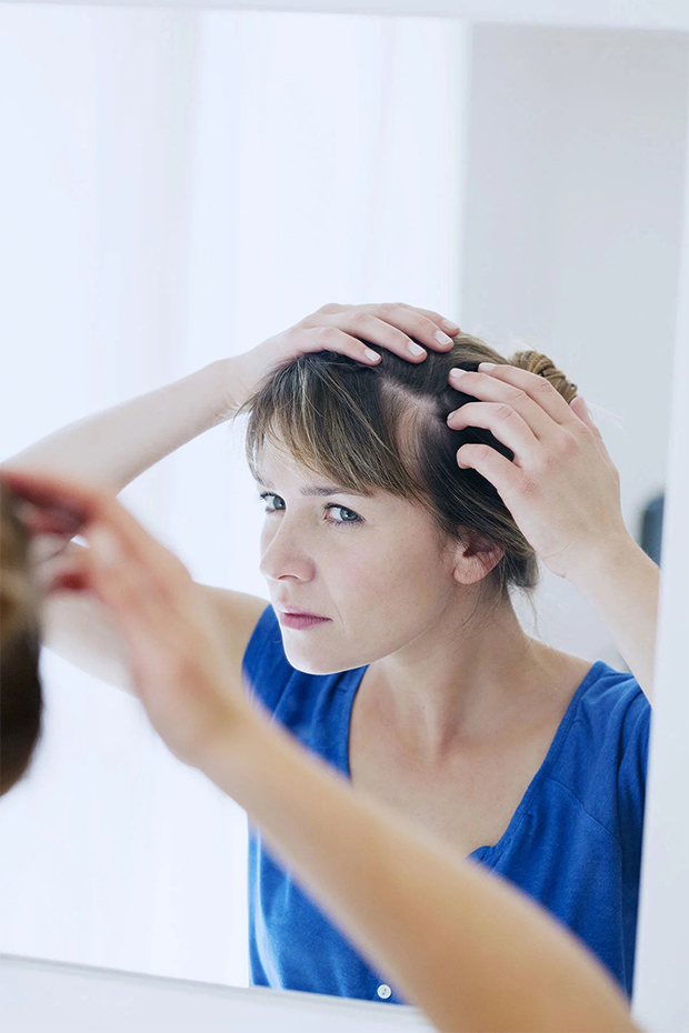 A confused woman checking her scalp in the mirror.