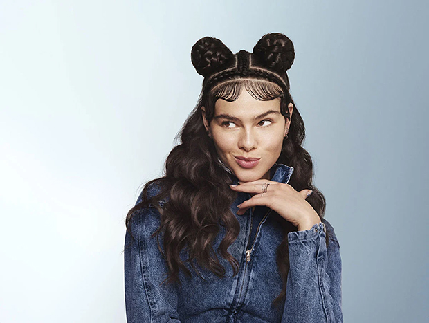 Young woman with long dark wavy hair partly pinned up in two buns is smiling.