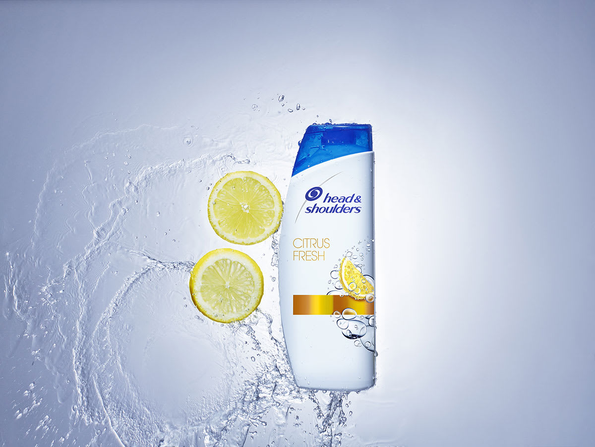A bottle of Citrus Fresh Head and Shoulders shampoo, composed with slices of lemon and a splash of water.