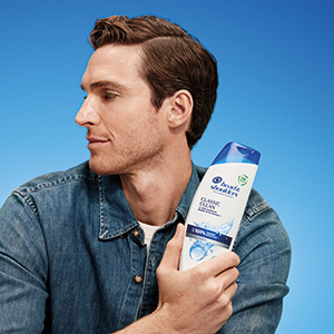 A man is holding a bottle of Head & Shoulders Classic Clean shampoo in his arms.