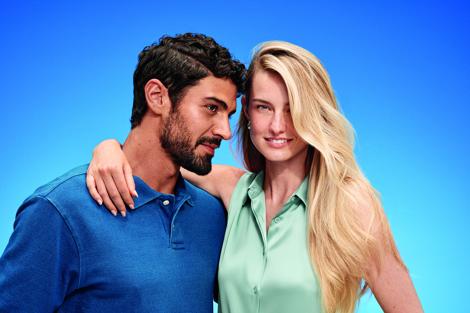 A man and a woman with healthy-looking hair pose together against a blue background.