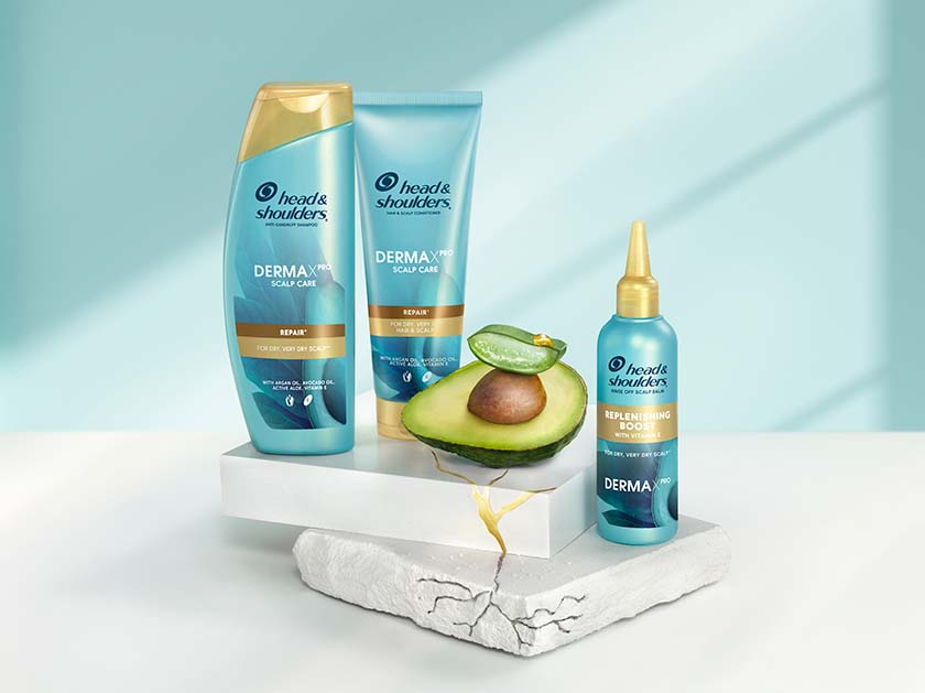 Derma X Pro Repairing Care Head & Shoulders shampoo, conditioner and scalp balm bottles, next to aloe and avocado pieces