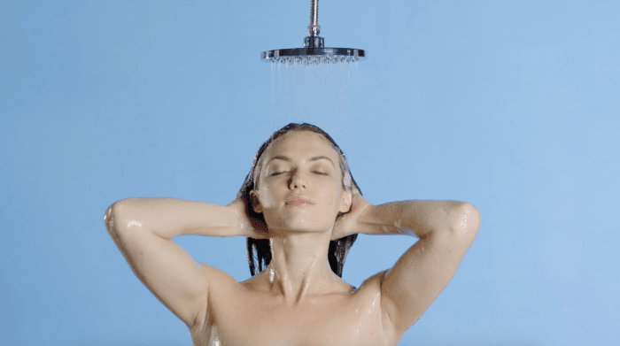 A woman taking shower on the light blue background - the shoulders and head frame view.