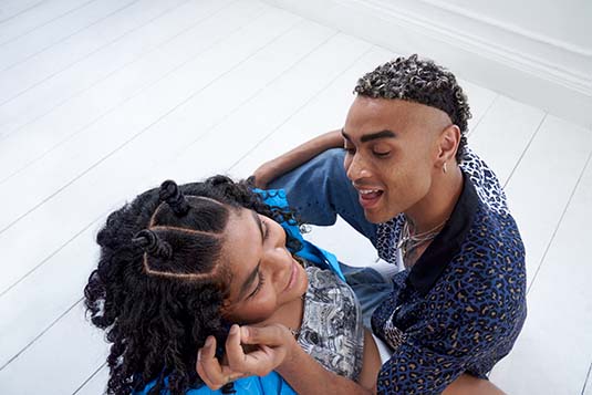 a woman and a men are sitting on the floor, the man is playing with the woman's curly hair