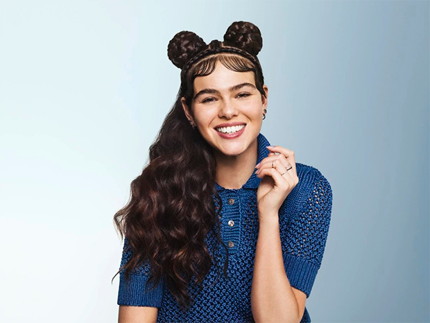 A young woman with a long curly dark hair partly pinned up in two buns smiling.