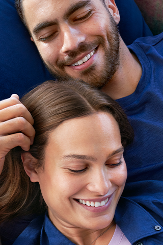 A man and a woman are lying on the sofa, stroking each other’s hair.