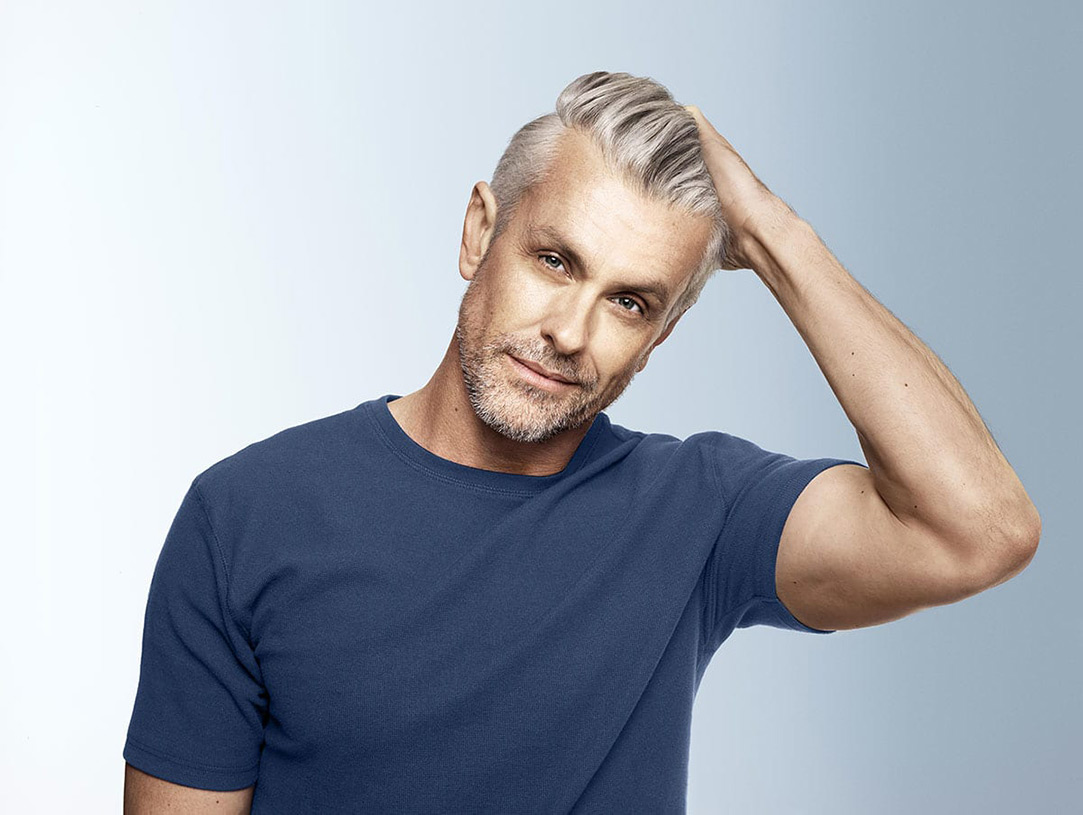 A mature man with grey hair and short beard fixing his stylish hairstyle.