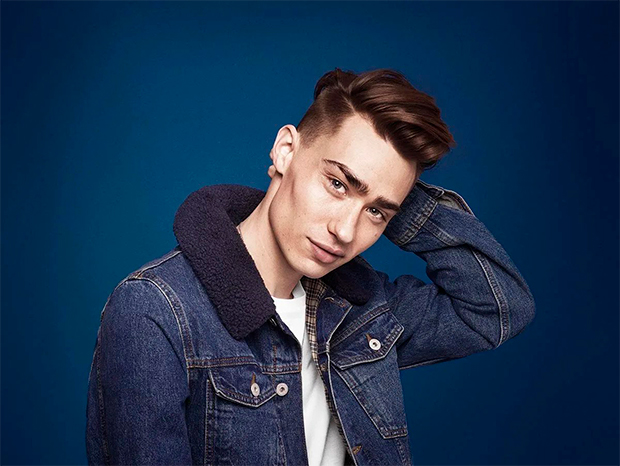 A young man with a modern hairstyle touching back of his head and looking straight ahead
