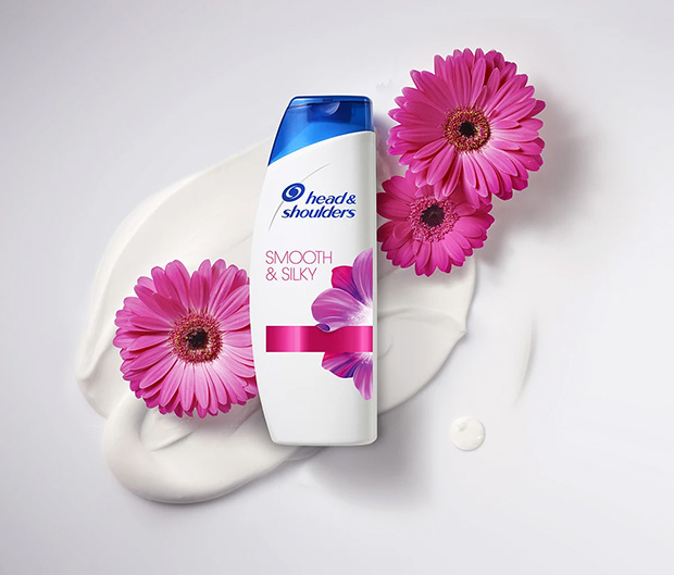 A bottle of Head & Shoulders Smooth & Silky shampoo laying next to beautiful pink flowers