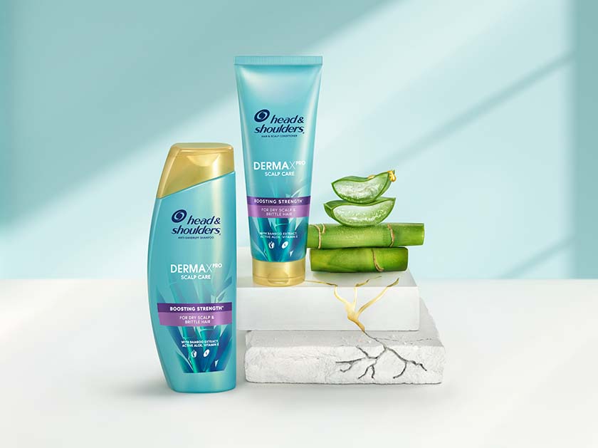 Derma X Pro Boosting strength Head & Shoulders shampoo and conditioner bottles, next to aloe and bamboo pieces