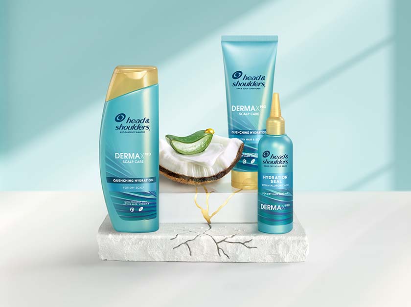 Derma X Pro Quenching Hydration Head & Shoulders shampoo, conditioner and scalp balm bottles, next to aloe and coconut pieces