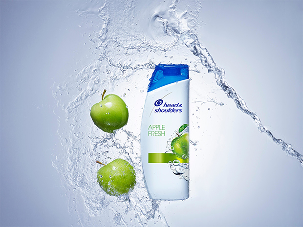 A bottle of Apple Fresh Head and Shoulders shampoo, composed with green apples and a splash of water.