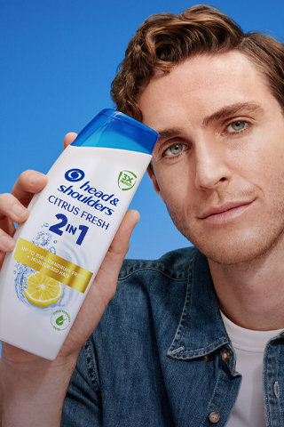 A man is holding a bottle of H&S Citrus Fresh 2 in 1 shampoo.