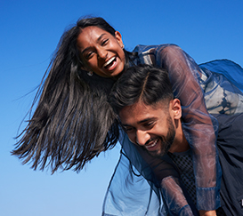 Man with black hair holds the woman with long black hair on a piggyback and they laugh