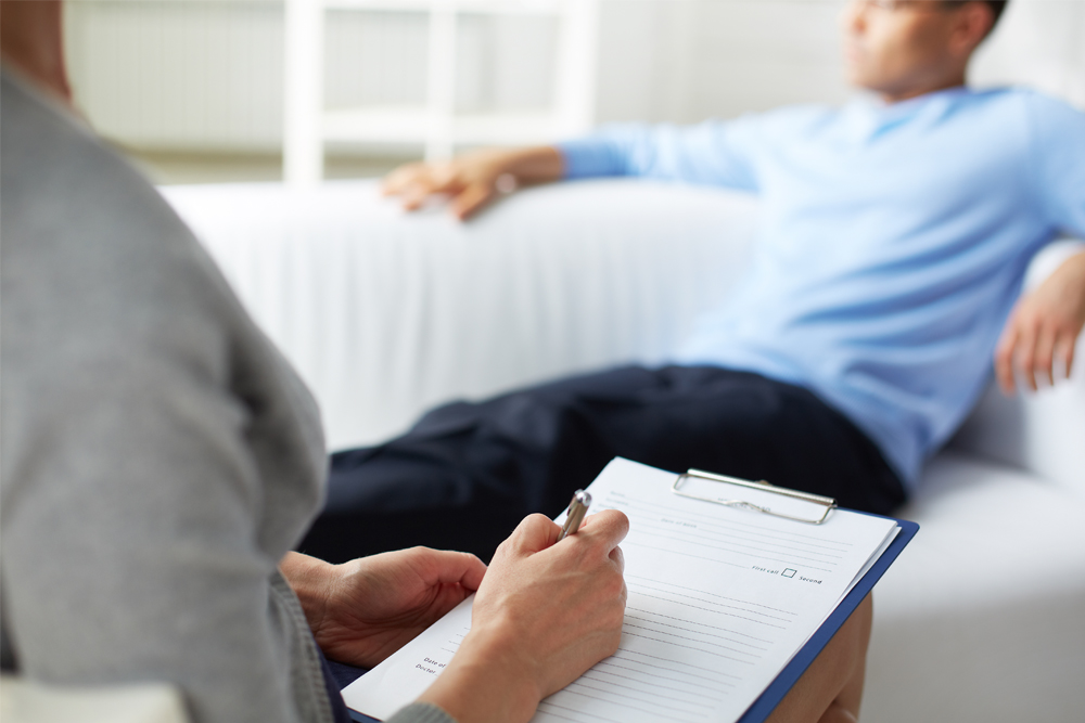 A man seated in a therapist's office while she takes notes