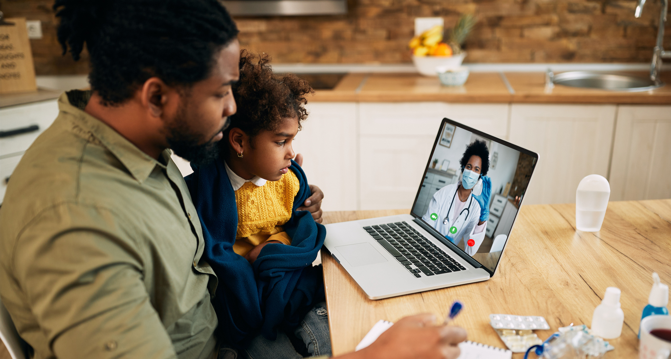 dad and daughter sitting at kitchen table during a telemedicine appointment