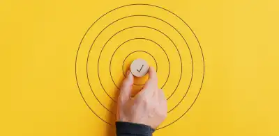 Male hand placing a wooden cut circle with check mark on it in the middle of drawn circles over plain yellow background.