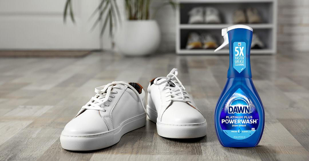 Zapatillas blancas sobre suelo de madera, y junto a ellas en el lado derecho se coloca el spray Dawn Platinum Plus Powerwash