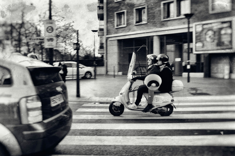Slightly antique tinted photograph of couple on Moped. The woman is carrying a lamp shade.